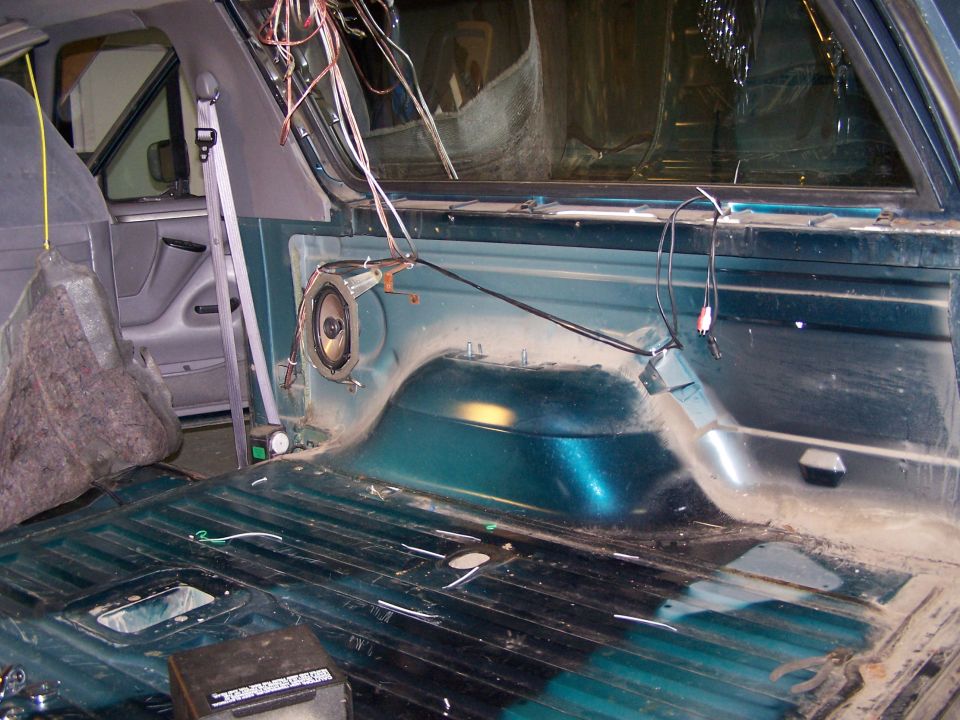 Interior of a vehicle, showing exposed wiring and a speaker mounted on the side panel. The floor is ribbed metal
