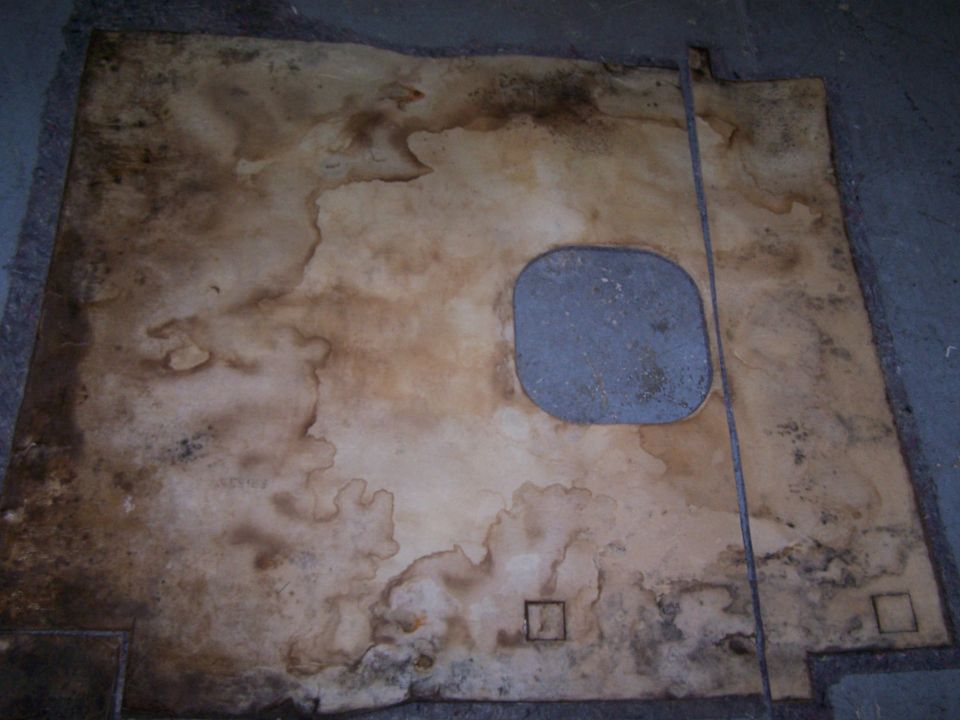 Worn carpet with water stains and a gray metal plate, showing two small square indentations