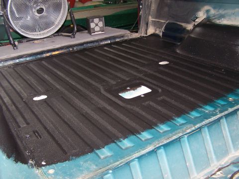 1995 Ford Bronco - Applying a bed liner to a truck bed. The ribbed surface and tie-down points are visible.