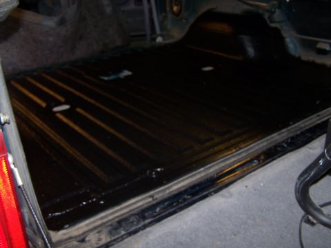 1995 Ford Bronco - The interior bed liner of a vehicle, showing a black surface with yellow stripes and some water droplets.
