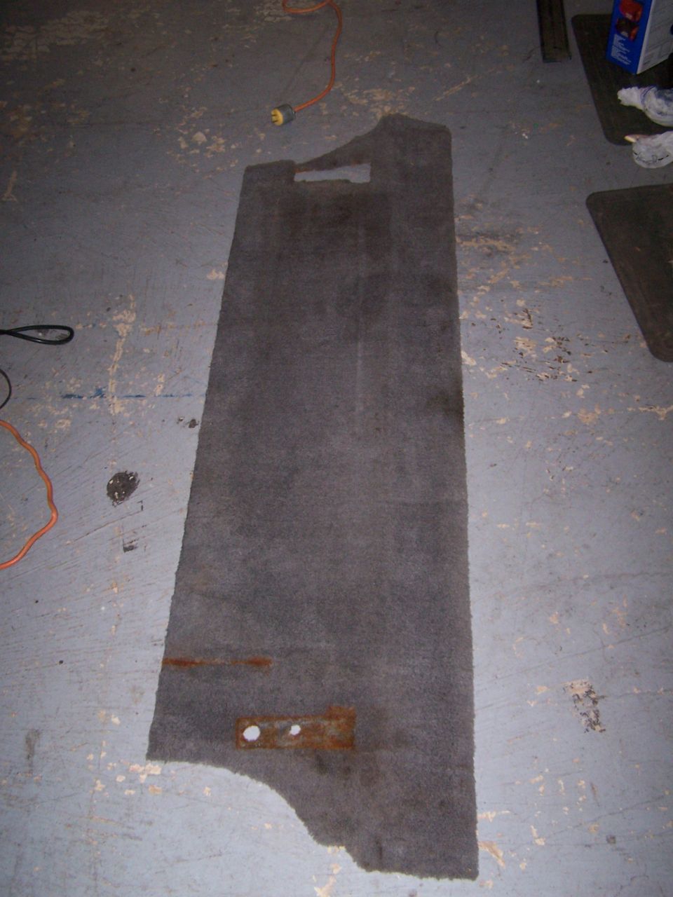 Gray carpeted floor mat with rust stains and two mounting holes