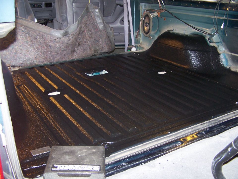 Interior of a vehicle's cargo area with a black bed liner and some insulation removed