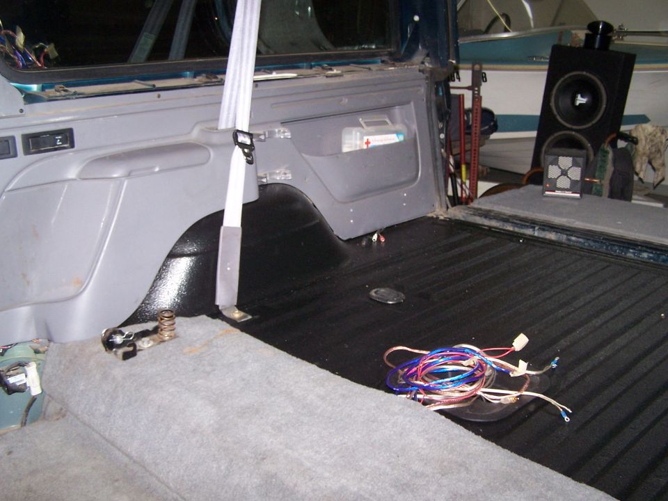 1995 Ford Bronco interior cargo area with black bed liner, gray carpet, seatbelt, first aid kit, and audio equipment