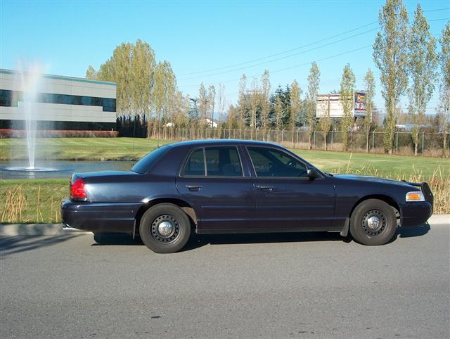 Dark blue Ford Crown Victoria police sedan side profile with black steel wheels