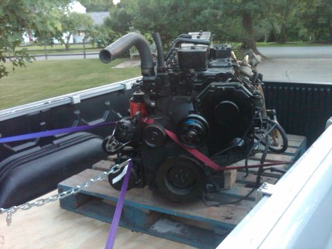1986 Ford Bronco - A black diesel engine is transported in the bed of a pickup truck, secured with straps and chains.