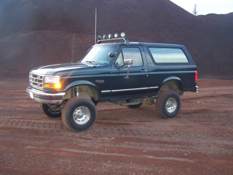 1995 Ford Bronco - This lifted 1995 Ford Bronco is shown in a three-quarter front view, parked on a dirt surface with a large pile of dark material in the bac…