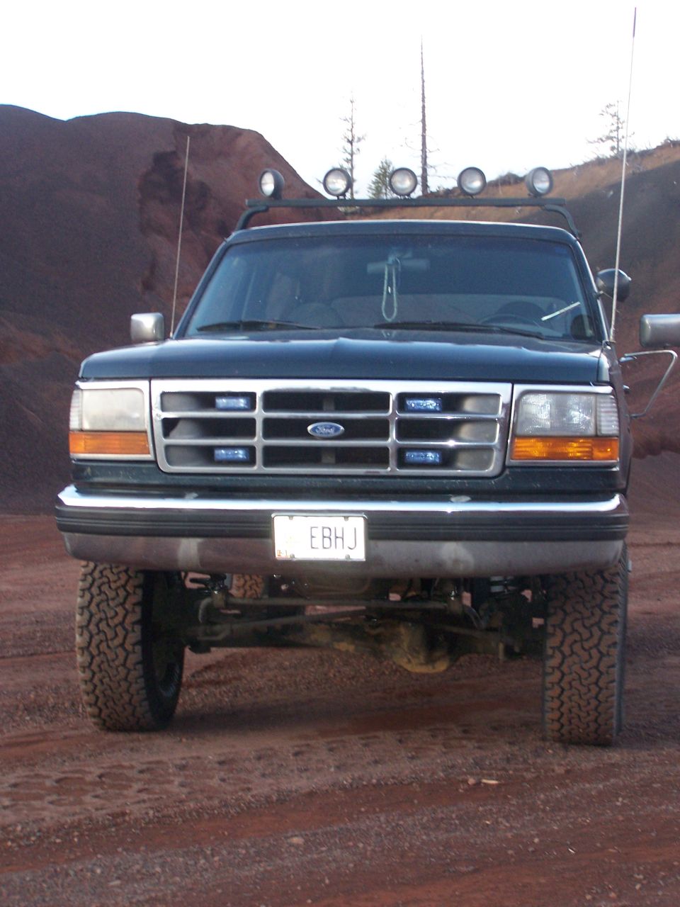 Front view of a dark green 1995 Ford Bronco with a lift kit and off-road lights on the roof rack