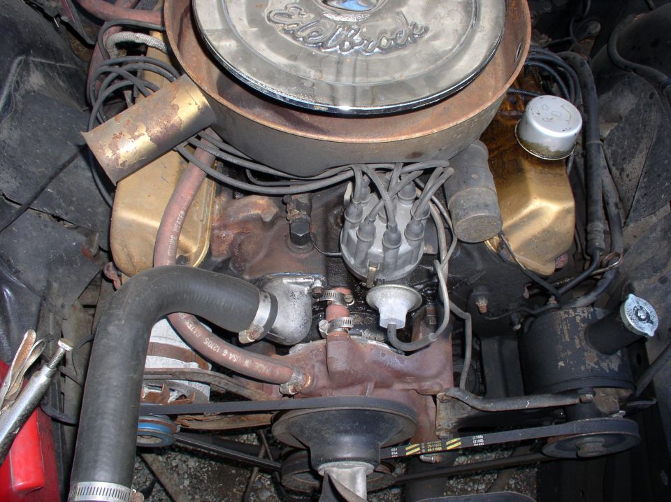 Dirty V8 engine bay with Edelbrock air cleaner, gold valve covers, and rusty components