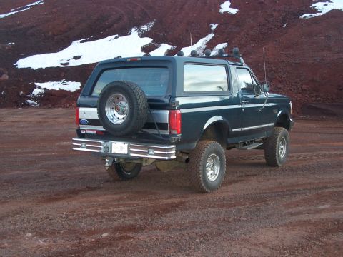 1995 Ford Bronco - This lifted Ford Bronco is parked on a dirt road with a snowy, rocky hill in the background.