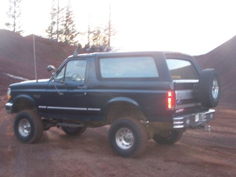 1995 Ford Bronco - This lifted Ford Bronco is shown from a three-quarter rear view, parked outdoors on a dirt surface.