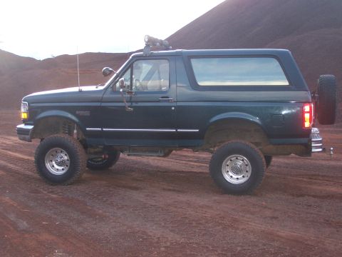 1995 Ford Bronco - A dark green Ford Bronco with a lift kit and off-road tires sits on a dirt road.