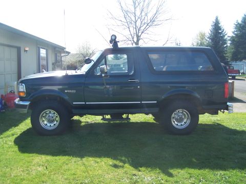 1995 Ford Bronco - Side profile of a lifted 1995 Ford Bronco parked on a grassy lawn.