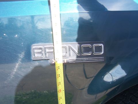 1995 Ford Bronco - A tape measure is held against the side of a teal vehicle, next to the "Bronco" emblem, likely measuring suspension lift.