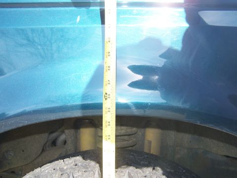 1995 Ford Bronco - Measuring the fender height of a vehicle with a tape measure. The suspension and tire are visible.