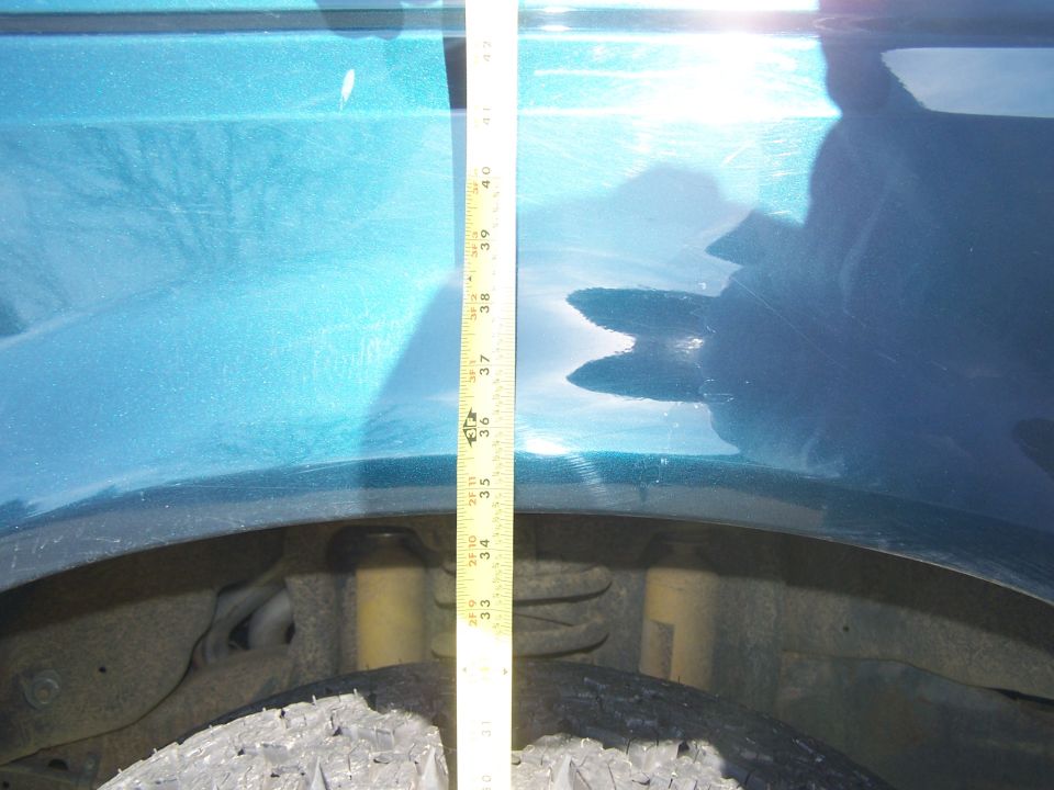 Measuring tape against teal vehicle fender, showing suspension and tire