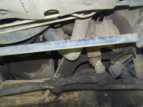 1995 Ford Bronco - Close-up of the dirty undercarriage of a vehicle, focusing on the steering and suspension system.