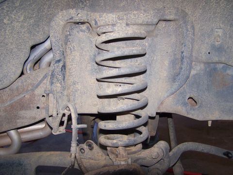 1995 Ford Bronco - This image shows a close-up of a vehicle's suspension system, including a coil spring and various linkages.