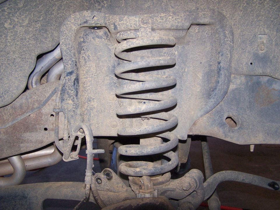 Close-up of dirty suspension coil and linkage with exhaust pipes visible