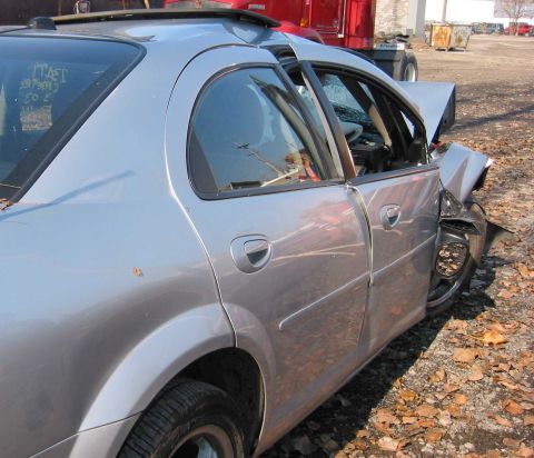 2001 Ford Taurus - A damaged silver sedan sits in a lot, its front end crushed and driver's side door open.