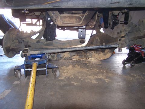 1995 Ford Bronco - The underside of a vehicle is shown with suspension components and lift kit parts, supported by jacks.