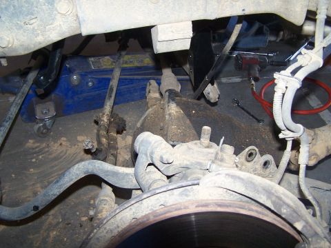 1995 Ford Bronco - Close-up view of vehicle suspension parts, including a brake rotor and linkage, with a hydraulic jack supporting the frame.