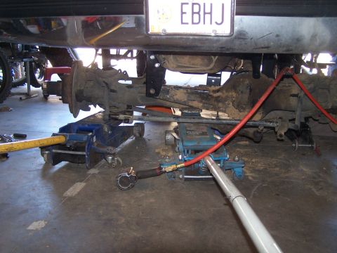 1995 Ford Bronco - The rear suspension and axle of a vehicle are supported by jacks and hydraulic lines in a garage setting.