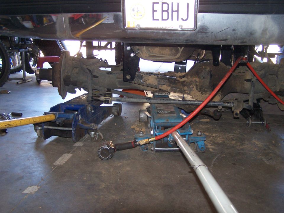 vehicle rear axle and suspension being worked on with jacks and tools