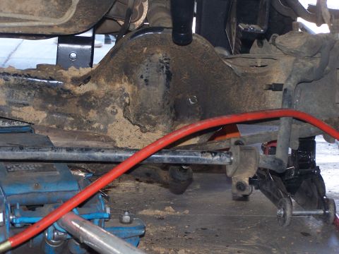1995 Ford Bronco - Close-up view of a vehicle's undercarriage, focusing on suspension parts and hydraulic jacks.