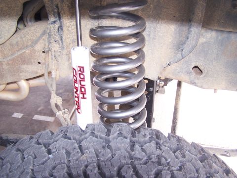 1995 Ford Bronco - Close-up of a vehicle's suspension system, a Rough Country shock absorber and a large coil spring over a tire.