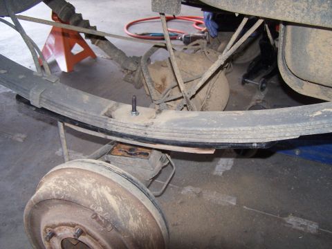 1995 Ford Bronco - Close-up view of a rear leaf spring suspension system, showing a lift block and drum brake assembly.