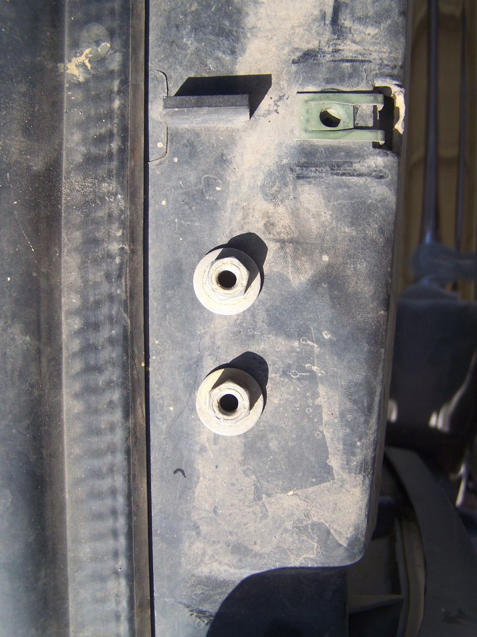 Close-up of a dark-colored vehicle part showing two bolts and a green clip fastener