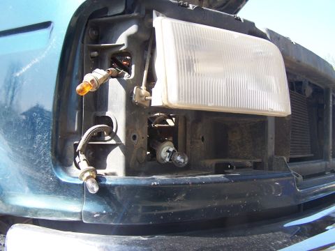 1995 Ford Bronco - The front headlight assembly of a vehicle is shown with exposed bulbs and wiring, indicating a repair or replacement is being worked on.