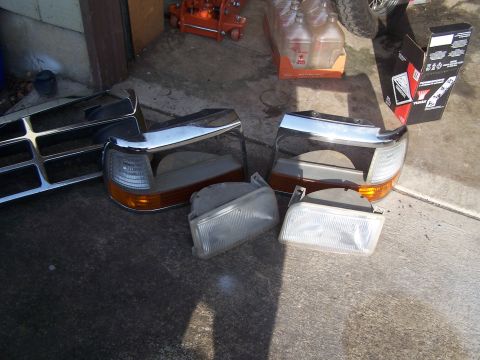 1995 Ford Bronco - Several vehicle lighting components and a section of a chrome grille are displayed on a concrete surface.