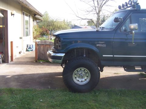 1995 Ford Bronco - A dark green Ford Bronco is parked on a driveway, showing its lifted suspension and missing grille.