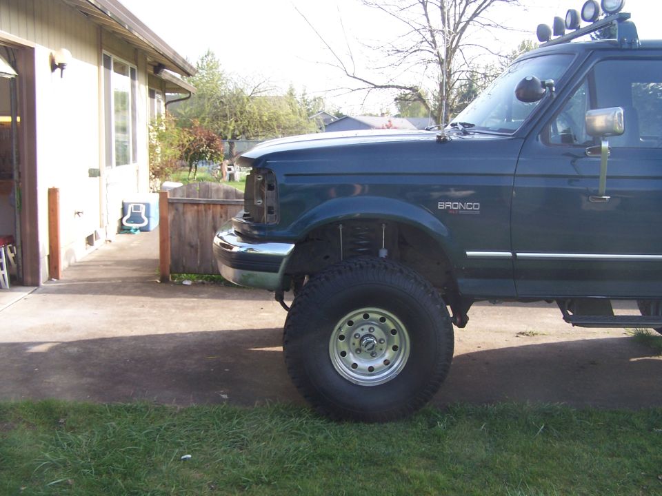 Dark green 1992 Ford Bronco with missing grille, lifted suspension, and off-road tires parked on a driveway