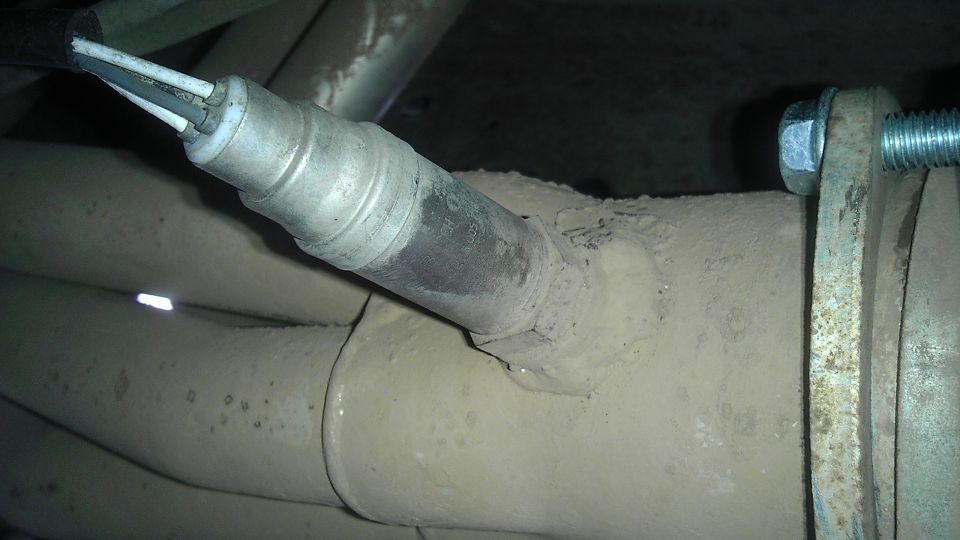 Close-up of an oxygen sensor screwed into a vehicle's exhaust manifold with wires connected