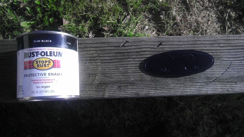 Black Ford oval emblem on weathered wood next to a can of Rust-Oleum flat black paint