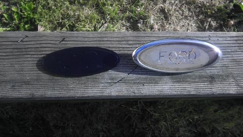 1995 Ford Bronco - A Ford oval emblem is shown next to a black oval emblem on a wooden surface.