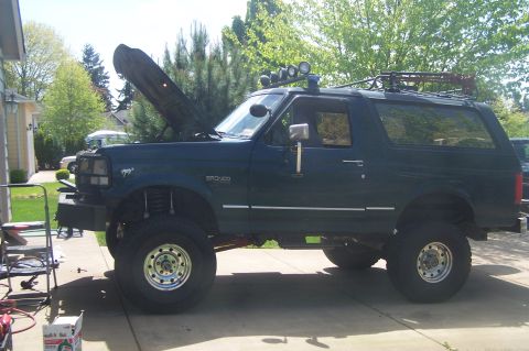 1995 Ford Bronco - A modified Ford Bronco sits in a driveway with its hood up, its lifted suspension and off-road accessories.