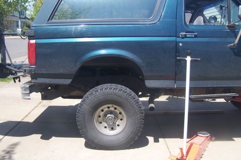1995 Ford Bronco - Side view of a teal SUV with a body lift, showing its lifted tire and a jack.