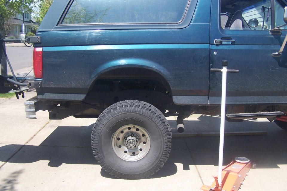 Teal SUV with a body lift, lifted tire, and a jack on the ground