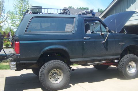1995 Ford Bronco - Side view of a dark green 1995 Ford Bronco, modified with a roof rack and auxiliary lights.