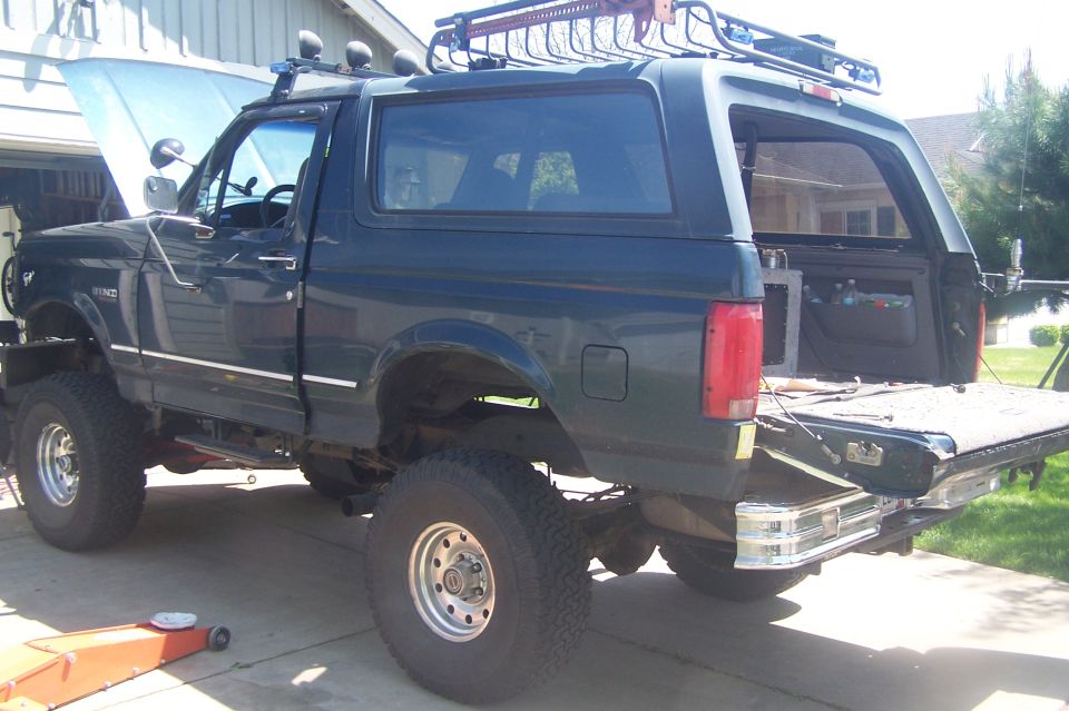 Dark green Ford Bronco with lifted suspension and roof rack. Hood is up, tailgate is open