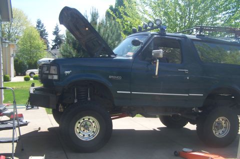 1995 Ford Bronco - A modified Ford Bronco with a body lift sits in a driveway with its hood up.