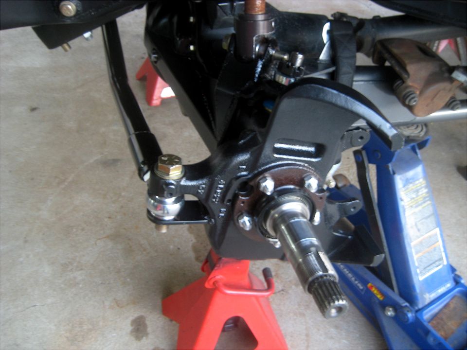 Close-up of a vehicle's steering knuckle, tie rod end, and brake caliper assembly supported by jack stands