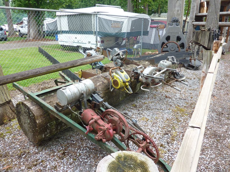 Old chainsaws and logging equipment on a trailer with a pop-up camper in the background