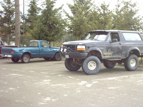 1995 Ford Bronco - A lifted 1995 Ford Bronco is parked in a lot next to a blue Ford Ranger pickup truck.