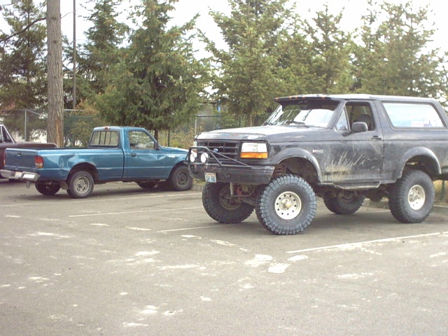 Black lifted Ford Bronco SUV on big tires beside a teal Ranger pickup in a parking lot
