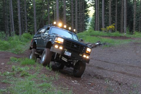 1995 Ford Bronco - This modified Ford Bronco navigates a muddy trail surrounded by tall trees.
