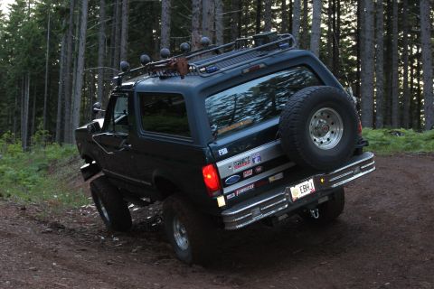 1995 Ford Bronco - This Ford Bronco is equipped with a roof rack and spare tire, navigating a wooded trail.